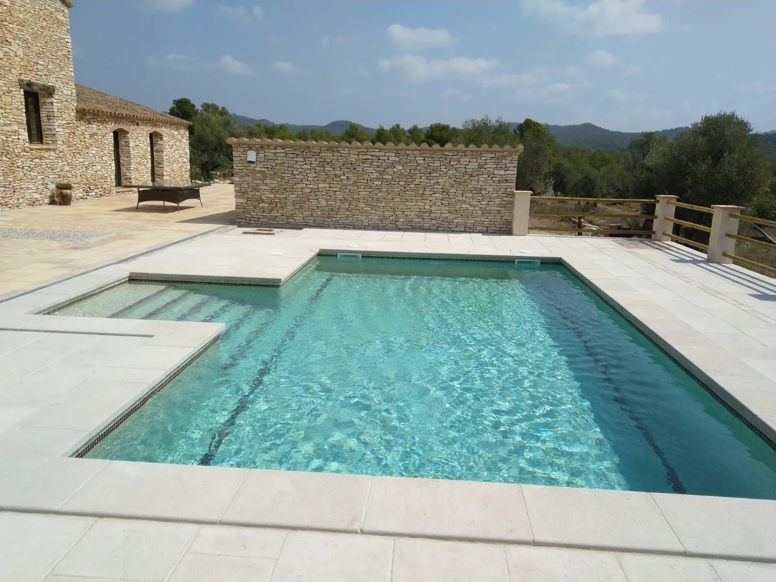 Piscina amb la vora de pedra i un mur de pedra seca al fons