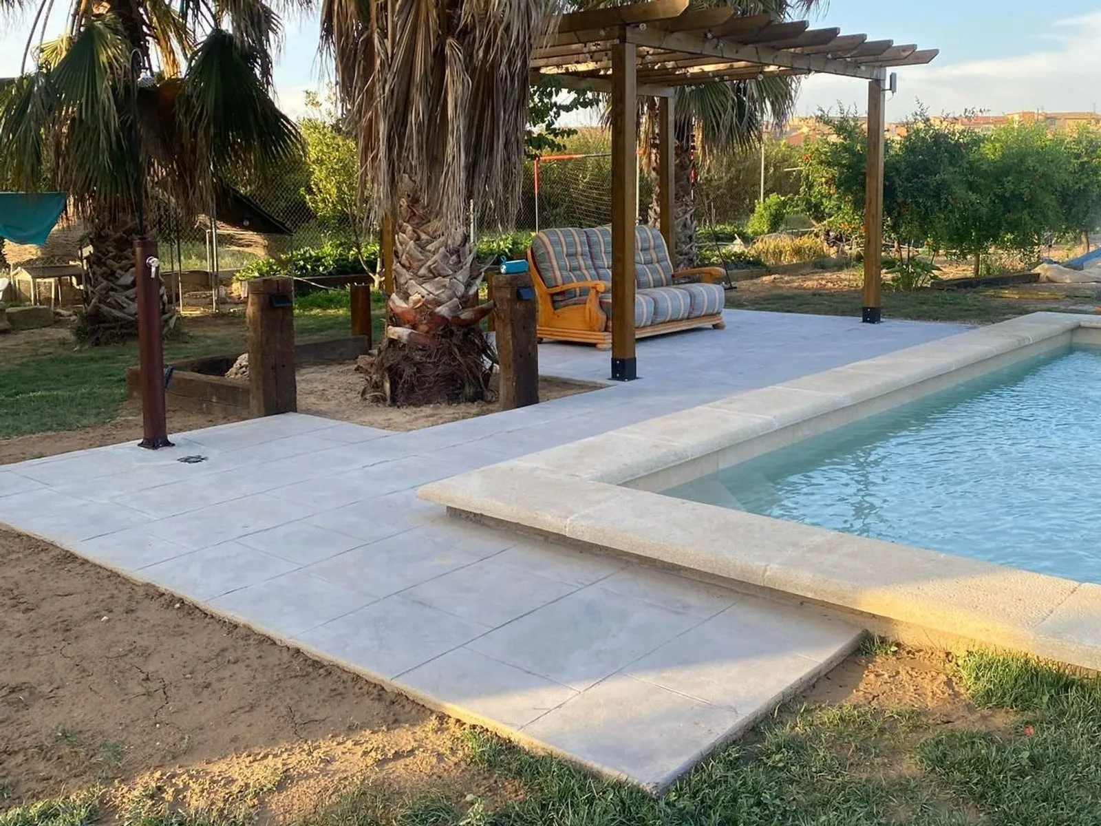 Piscina amb el paviment de pedra i una pèrgola de fusta al costat